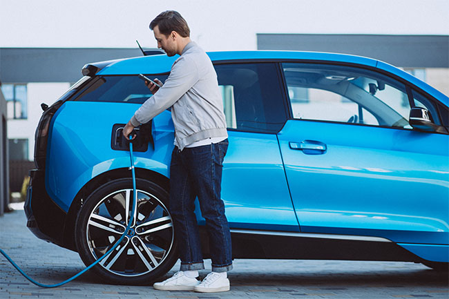 Man charging electric vehicle and managing charge with phone app. 