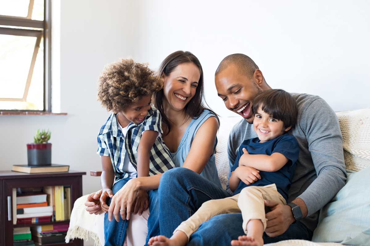 smiling male and female parents with 2 young children on a couch