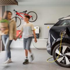 electric vehicle plugged into family garage with mother and son walking in the foreground.